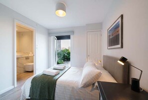 A modern bedroom with a bed, bedside tables, a nightstand, a lamp, and a window. - Rampart View -  a house that sleeps 6 guests  in 3 bedrooms (Gosport)