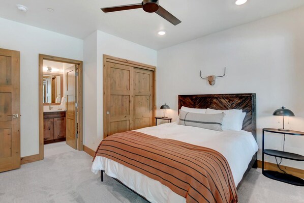 A bedroom with a large bed, wooden wardrobe, and a ceiling fan.