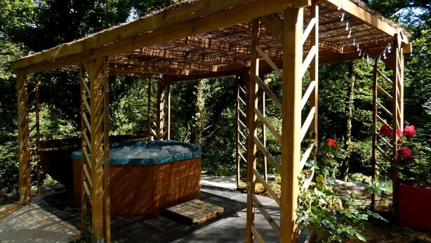 Un belvédère en bois doté d’un jacuzzi, entouré d’une végétation luxuriante et de fleurs rouges.