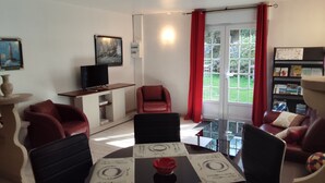 Un salon comprenant une table à manger dressée pour quatre personnes, un téléviseur, un fauteuil rouge et une bibliothèque.