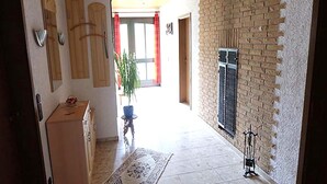 Un pasillo con suelo de baldosas, una planta en maceta, una mesita y un tapete decorativo.