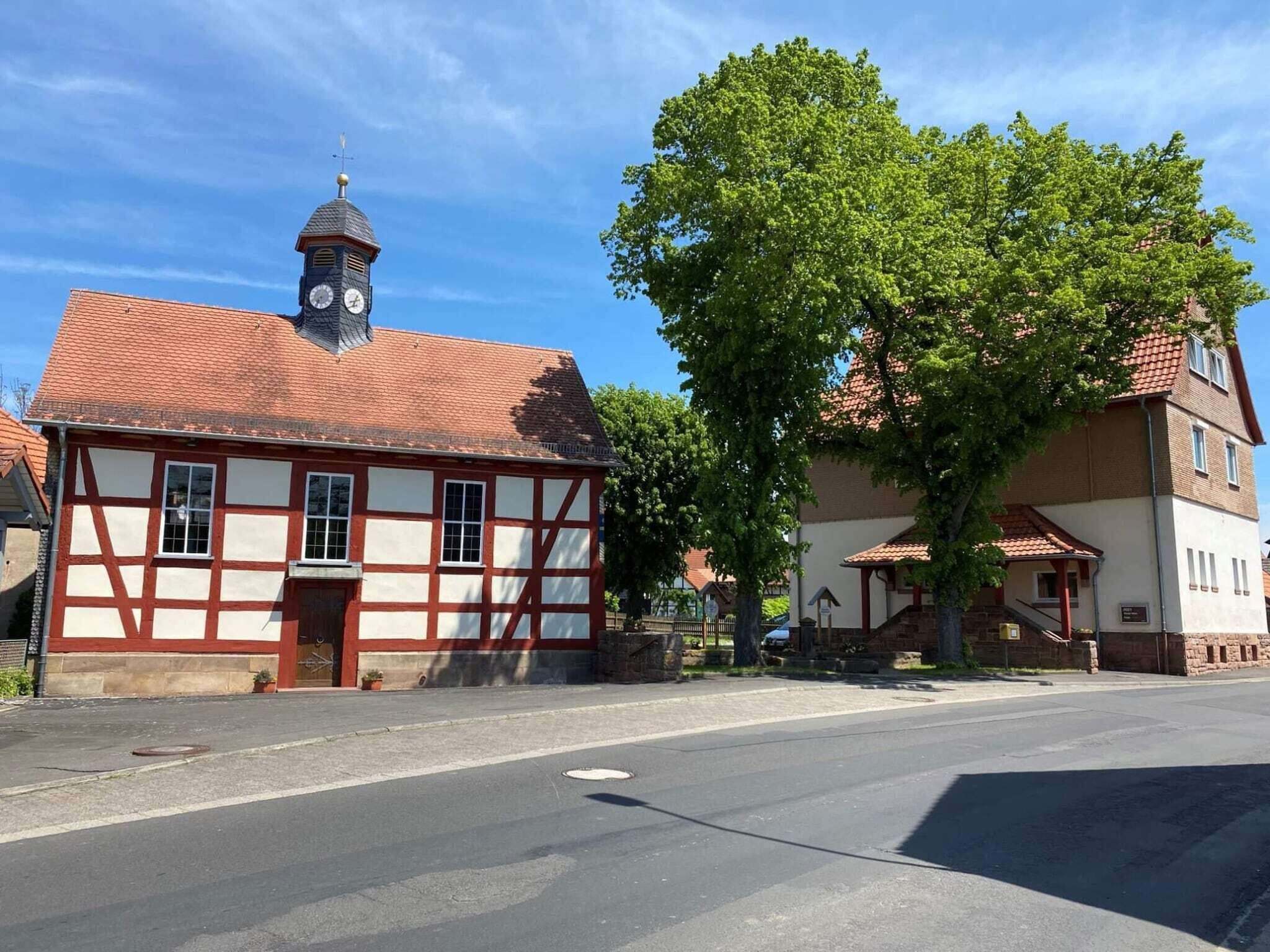 Un bâtiment traditionnel à colombages, doté d’une tour horlogée, d’un grand arbre devant et surplombé d’un ciel dégagé.