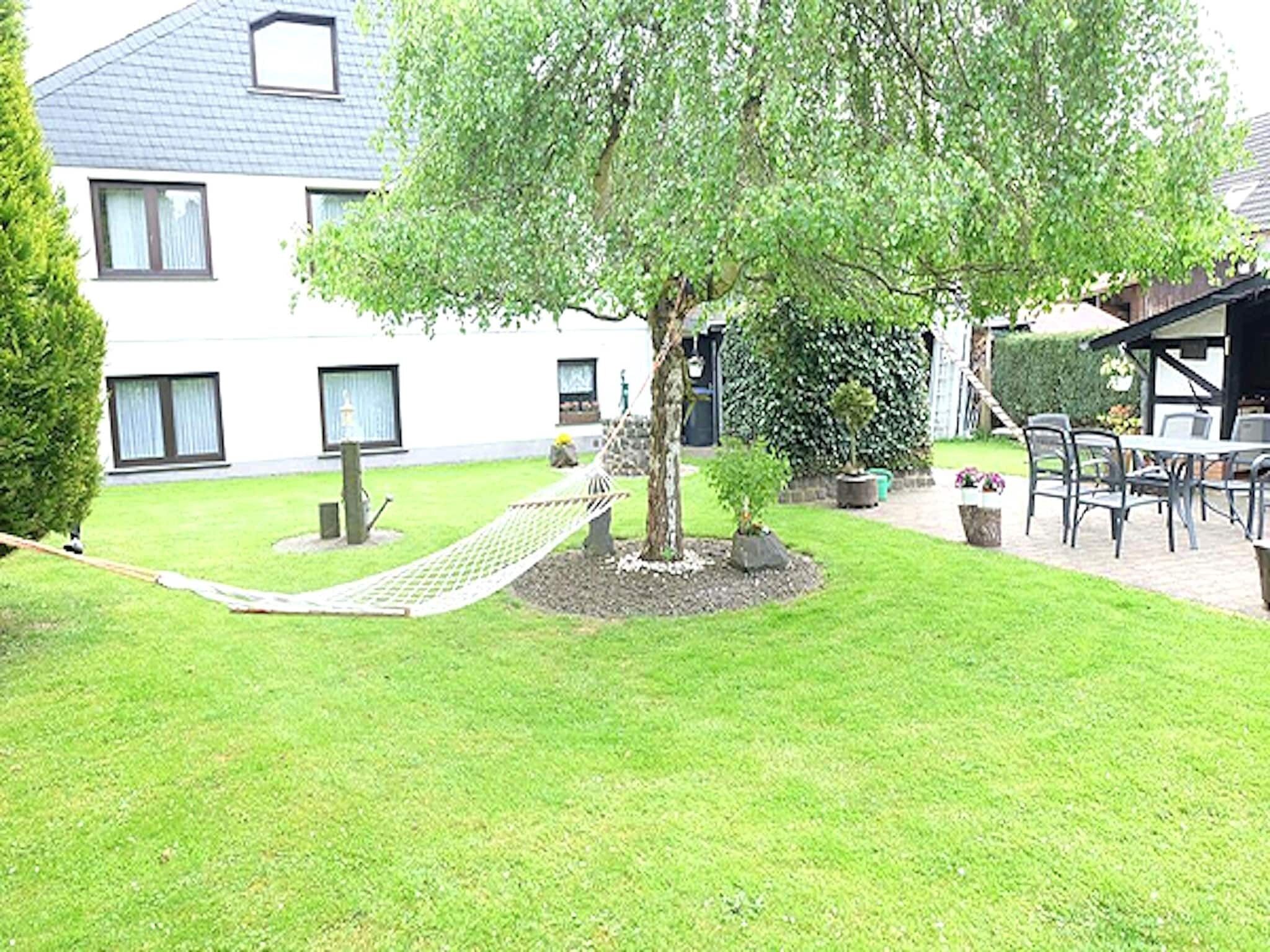 A well-maintained garden with a hammock, a small tree, and a patio area with outdoor furniture.
