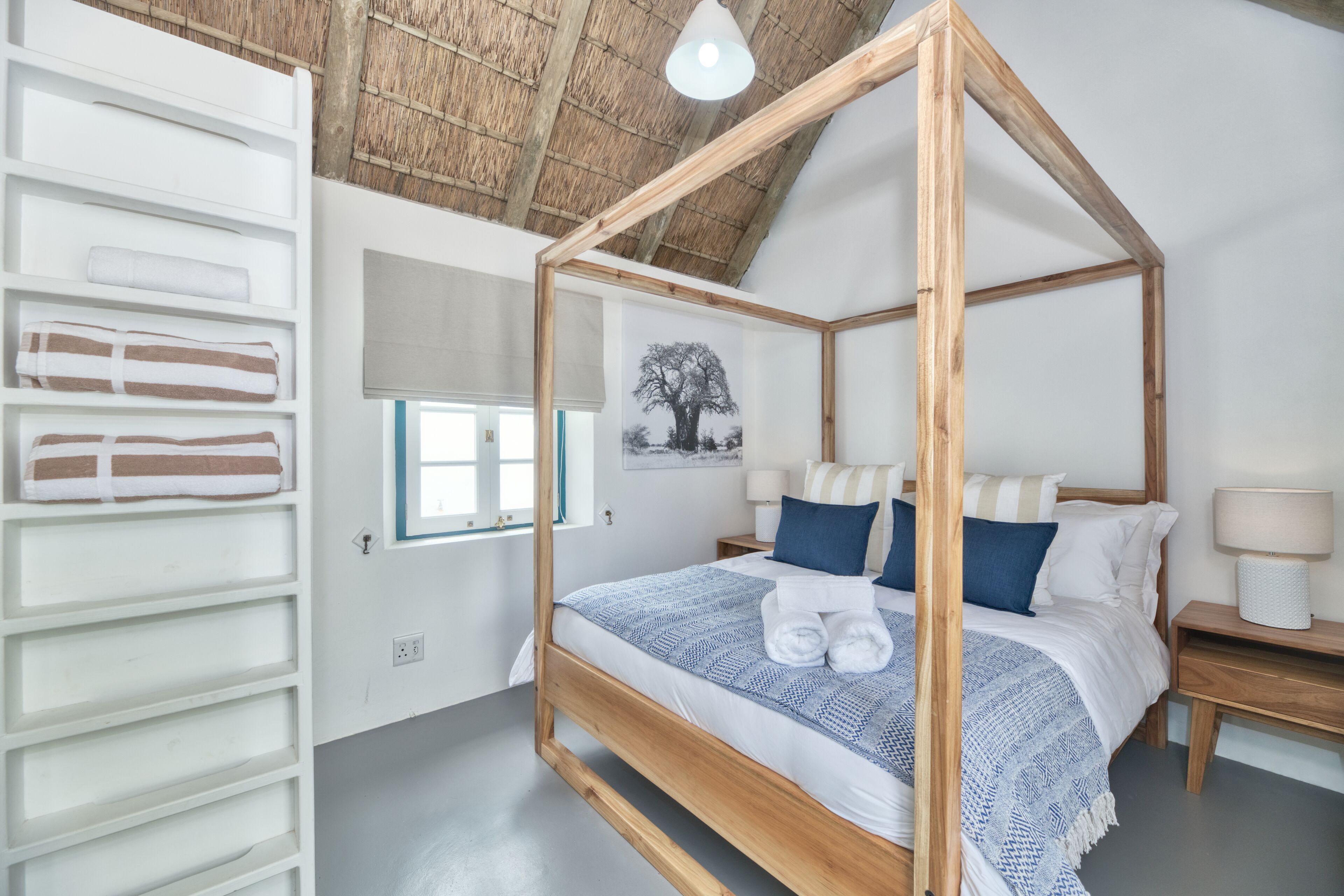 Un lit à baldaquin avec une structure en bois, une table de chevet blanche avec une lampe et une étagère murale avec des serviettes.