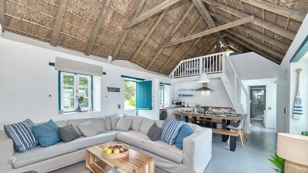 A modern living room with a large sectional sofa, a wooden coffee table, and a dining area with a wooden table and chairs.
