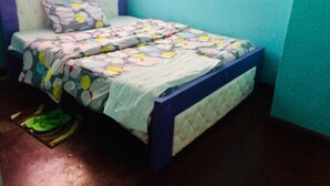Una cama individual con una colcha estampada, un almohadón y un cabecero azul en una habitación con paredes verde mar.