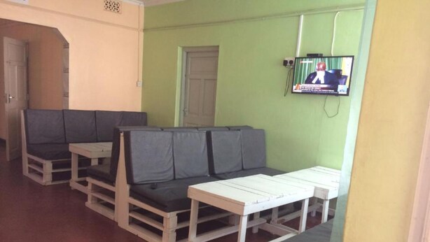 Ein Sitzbereich mit gepolsterten Bänken und Tischen, einem an der Wand befestigten Fernseher und einer Tür im Hintergrund.