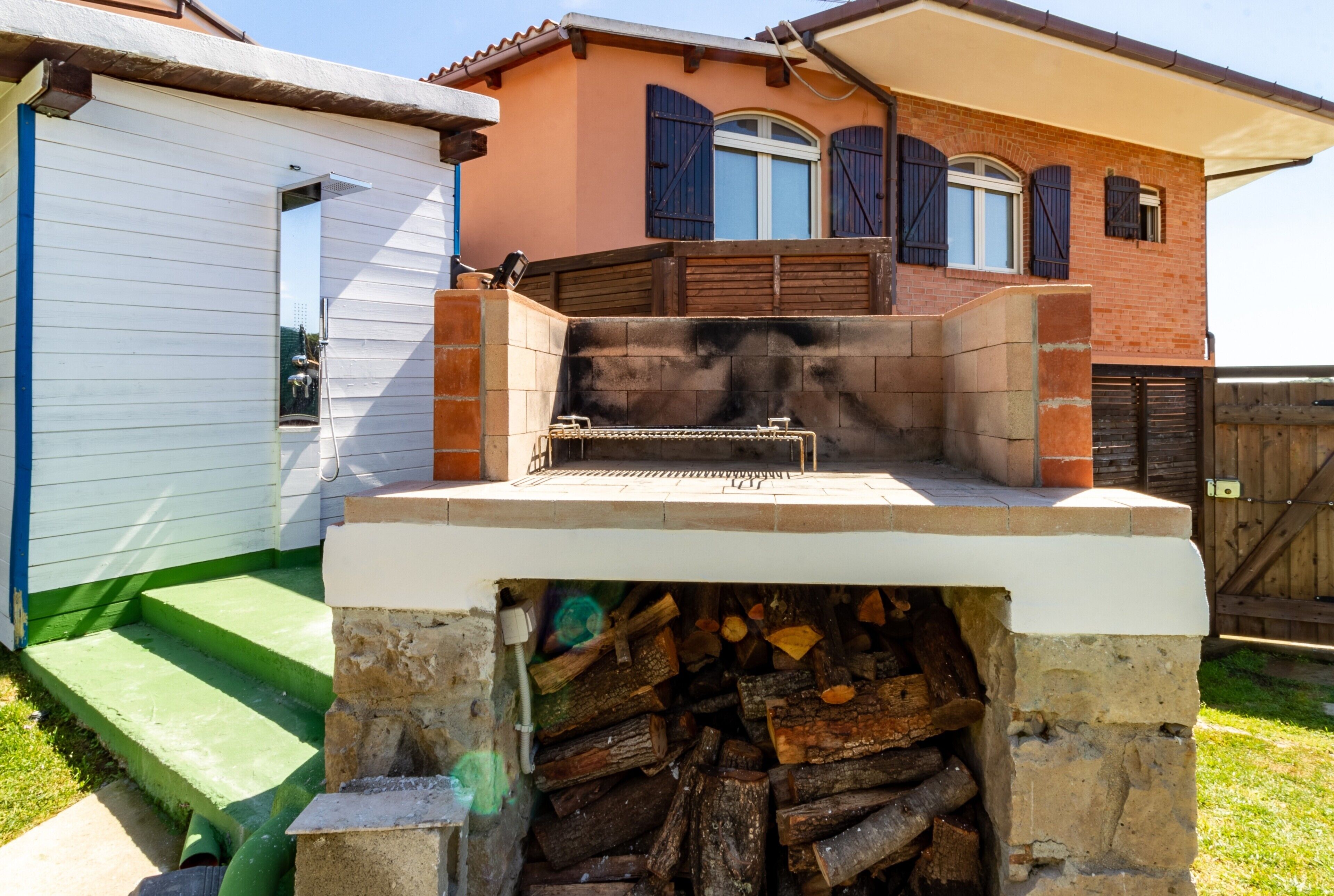 Un espace patio avec un barbecue, des marches menant à une maison et une pile de bois de chauffage.