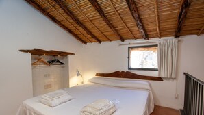 Ein Schlafzimmer mit Bett, einem Fenster mit Vorhängen, einem hölzernen Regal mit Kleiderhaken und einer Lampe.