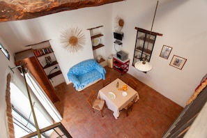 Un espace repas comprenant une table, des chaises, un canapé bleu, une bibliothèque, des éléments décoratifs muraux et une fenêtre.