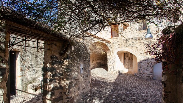 Ein steinerner Innenhof mit Bögen, einer Holztür und einem Kopfsteinpflasterboden.