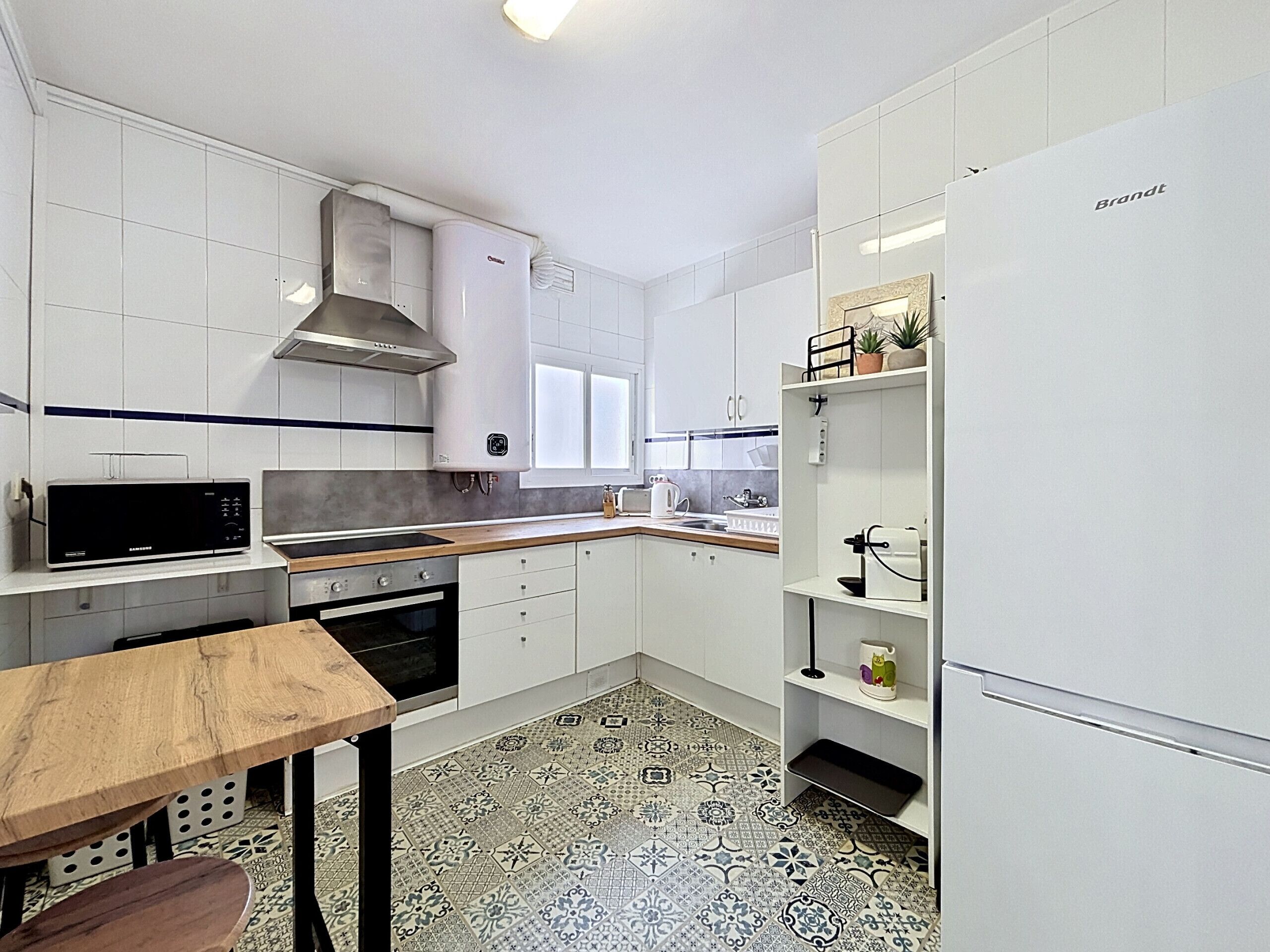 Een moderne keuken met witte kastjes, een roestvrijstalen afzuigkap, een magnetron, een oven en een koelkast.