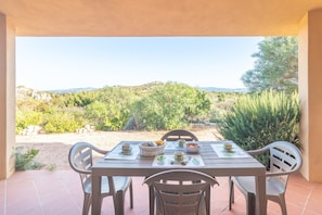 Une table de patio avec des chaises, un panier et un saladier, donnant sur un paysage naturel composé d’arbres et de collines.