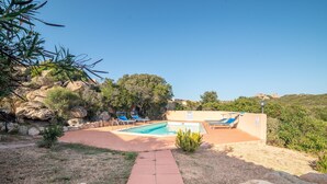 A pool area with lounge chairs, a clear sky, and a rocky landscape.