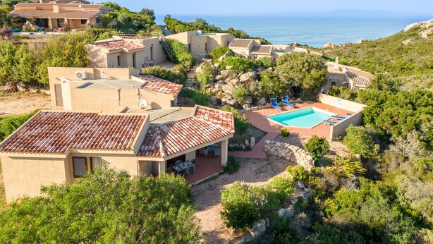 A coastal villa with a swimming pool, terraced roofs, and a view of the sea.