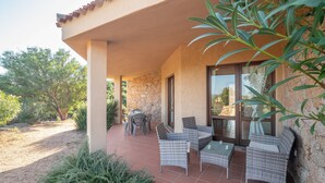 A covered patio with wicker furniture, a stone wall, and a view of the interior through glass doors.