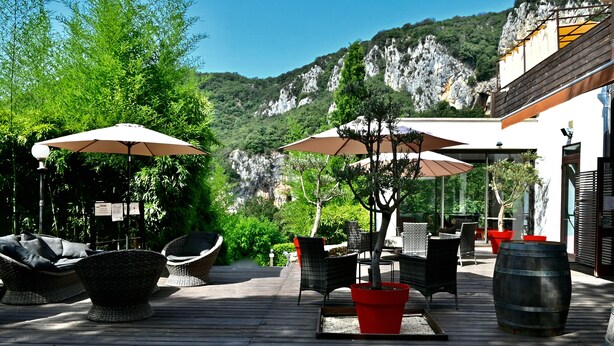 An outdoor patio with wicker furniture, umbrellas, and potted plants. - Hotel Restaurant le Belvedere (Vallon-Pont-d'Arc)