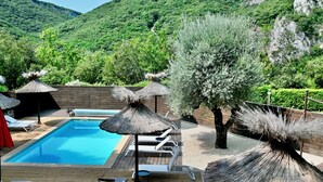 A wooden deck with a swimming pool, lounge chairs, and thatched umbrellas. - Hotel Restaurant le Belvedere (Vallon-Pont-d'Arc)
