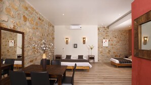 A hotel room with a stone wall, a wooden dining table with chairs, a bed with a wooden frame, and a red accent wall. - Hotel Restaurant le Belvedere (Vallon-Pont-d'Arc)