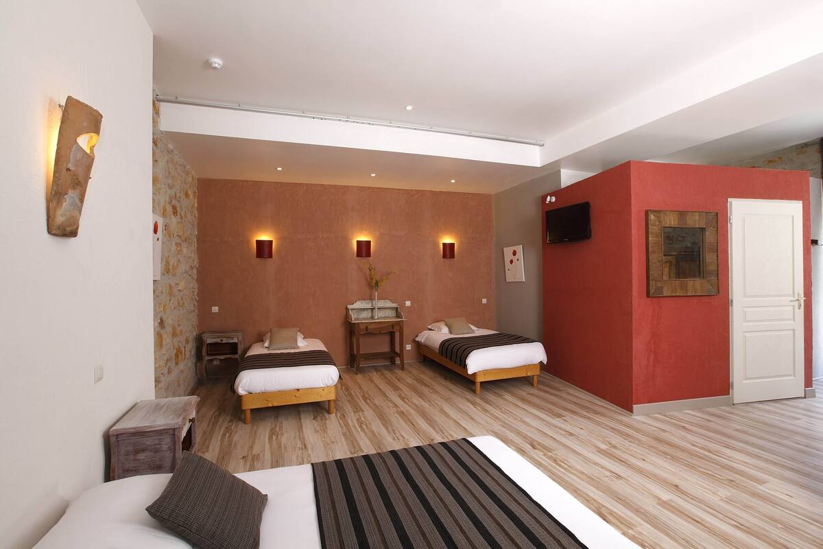 Une chambre d’hôtel avec deux lits, une petite table sur laquelle se trouve un vase, et un téléviseur fixé au mur.
