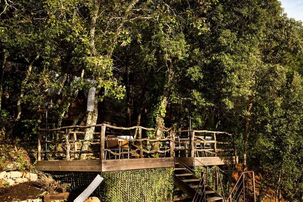 A wooden platform with chairs and a staircase, surrounded by dense forest.