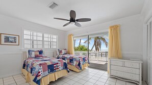 A bedroom with two beds, a ceiling fan, a window with shutters, and a view of the outdoors.