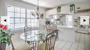A modern kitchen with white cabinets, a glass dining table, and a chandelier.
