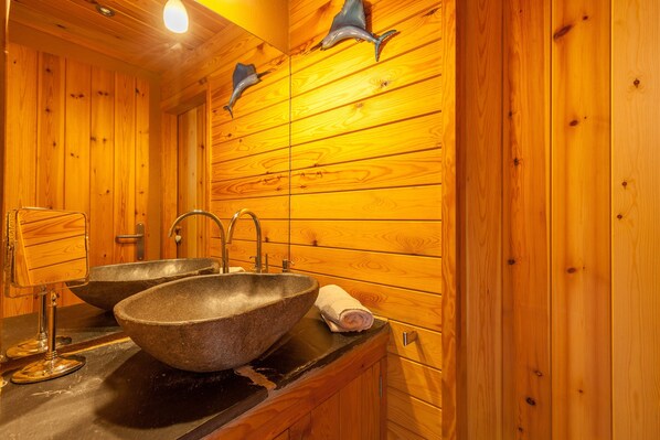 A wooden cabin bathroom with two sinks, a mirror, and wooden walls.