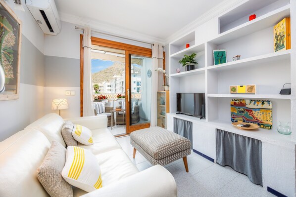 A modern living room with a sofa, ottoman, TV, and shelves with decorative items.