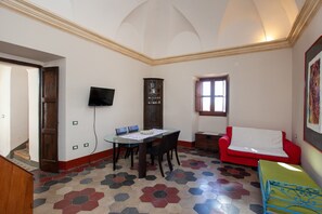 A room with a dining table, chairs, a red sofa, a television, and a cabinet.