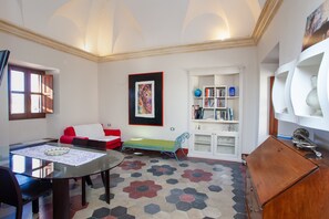 A room with a glass dining table, a red sofa, a green bench, a white bookshelf, and a cabinet.