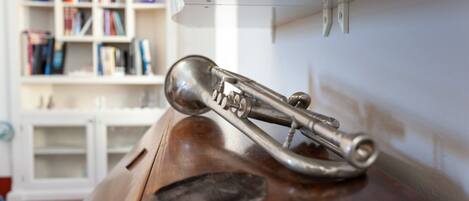 A brass trumpet on a wooden surface, a white shelf with books, and a white cabinet in the background.