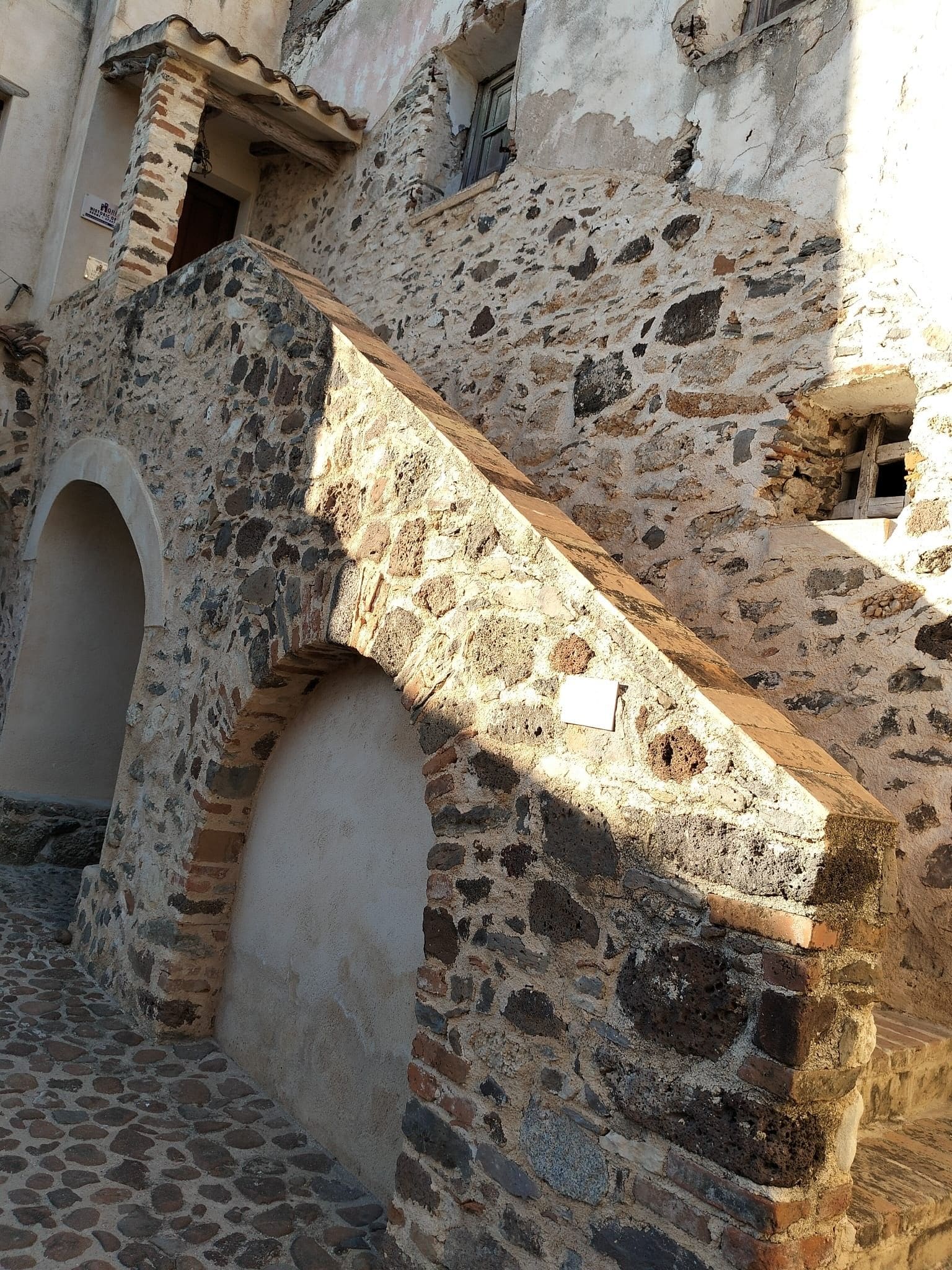 A stone staircase leading to an arched doorway, part of an old building with visible wear and repair.