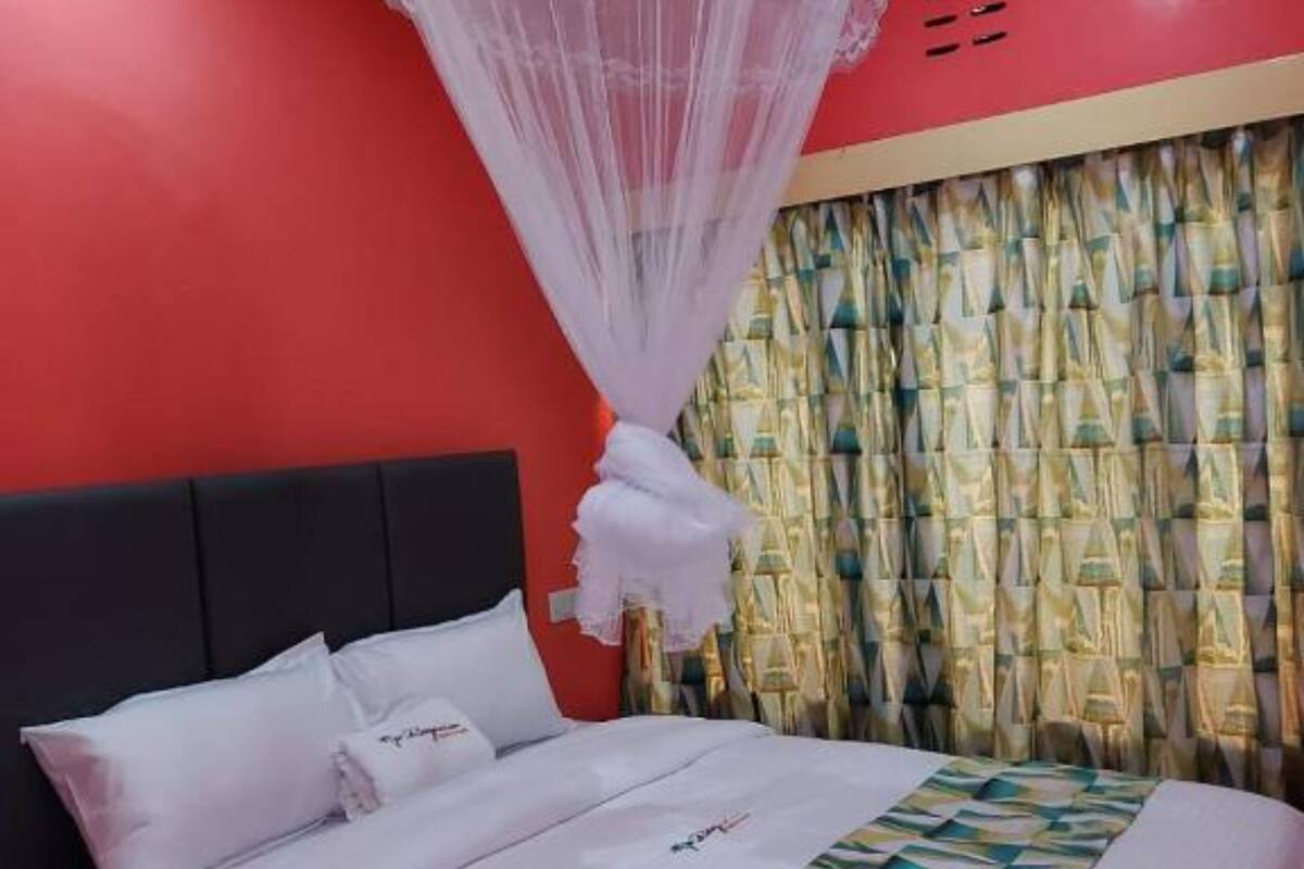 Una habitación de hotel con una cama, ropa de cama blanca, dosel y cortina con diseño geométrico.