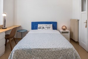 Une chambre à coucher comprenant un lit, un bureau, une chaise, une table de chevet et une lampe.