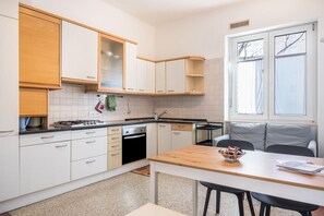 A modern kitchen with white cabinets, a wooden countertop, a gas stove, and a dining area with a table and chairs.