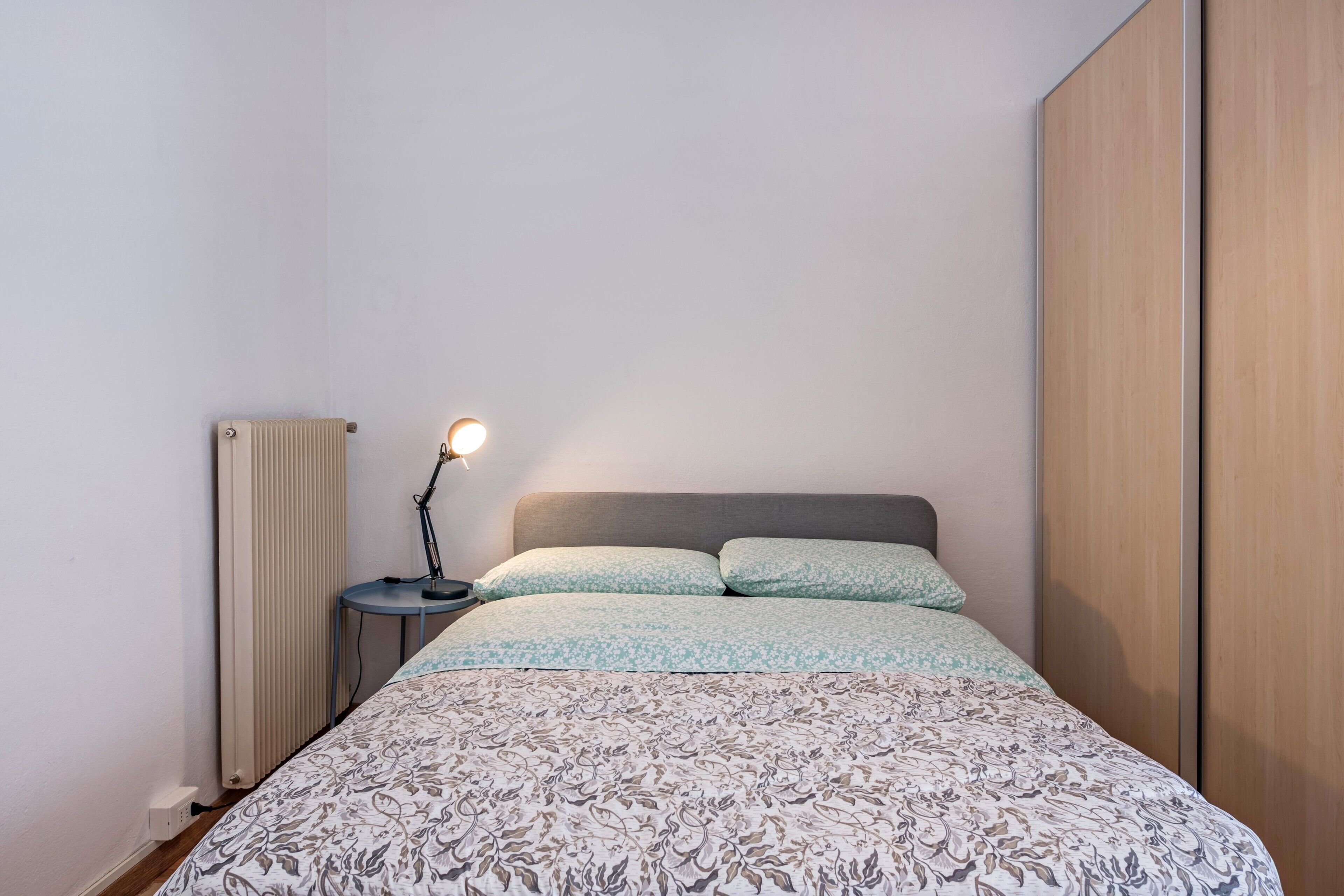 Ein Schlafzimmer mit Bett, Nachttischlampe, Heizkörper und einem Kleiderschrank.