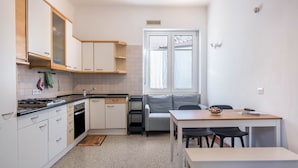 Cocina compacta con armarios blancos, estufa y comedor con mesa y sillas.