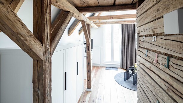 A modern kitchen with wooden beams, white cabinets, and a wooden wall panel. - Apartment 1 Wohnen am Turm - Living at Schloßplatz (Oldenburg)
