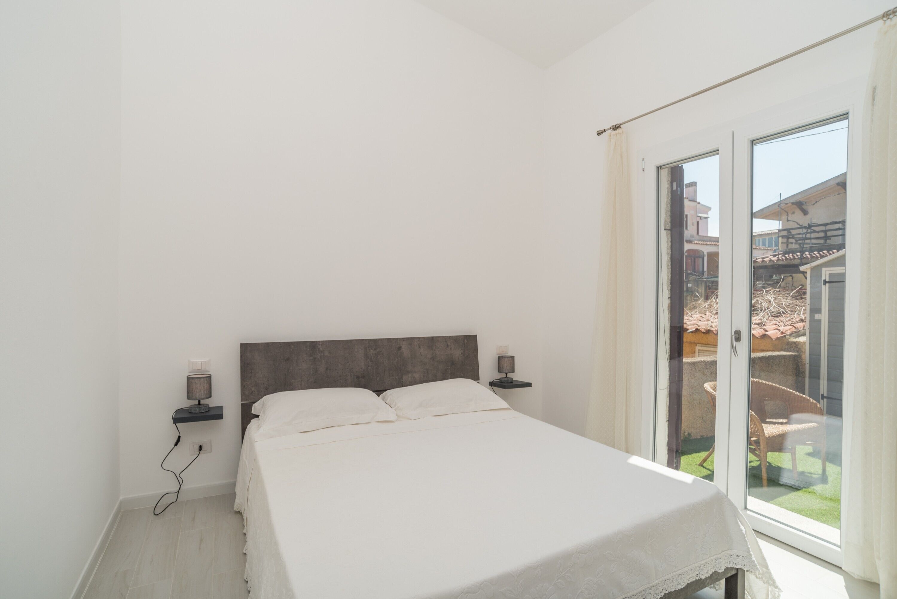 Une chambre à coucher comprenant un lit, des lampes de chevet, une table de chevet et une porte-fenêtre coulissante donnant sur un espace extérieur.