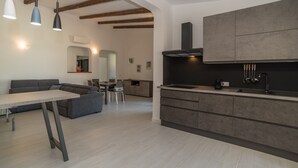 Una cocina moderna con armarios empotrados, un rincón comedor con sofá y mesa, y vigas de madera a la vista en el techo.