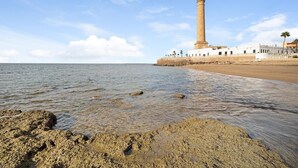 A coastal scene with a lighthouse, sandy beach, and rocky shoreline. - Apartment Caepionis close to the Beach with Shared Rooftop Terrace & Wi-Fi (Chipiona)