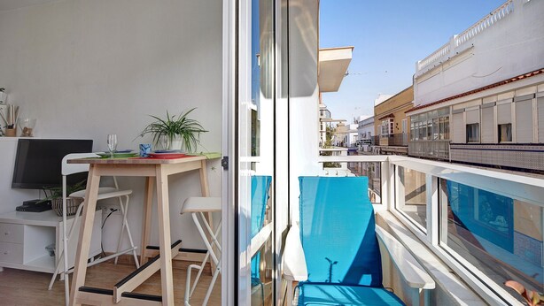 A balcony with a blue awning, a small table with a plant, and a TV on a stand. - Apartment Caepionis close to the Beach with Shared Rooftop Terrace & Wi-Fi (Chipiona)
