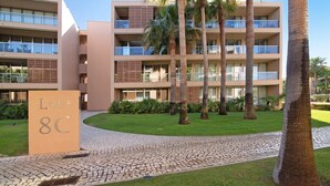 A multi-story hotel with a paved entrance, palm trees, and a sign reading 'Lote 8C'. - Apartamento Salgados Sol e Sal with Pool, Wi-Fi, A/C & Garden (Guia)