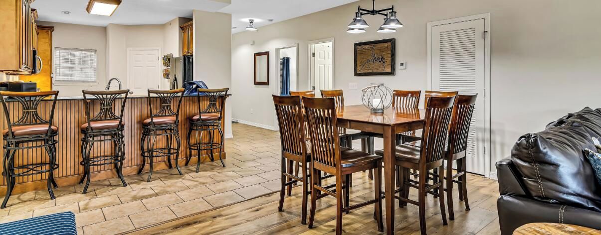 A spacious living area with a wooden dining table and chairs, a bar area with stools, and a leather couch.