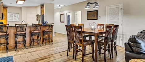 A spacious living area with a wooden dining table and chairs, a bar area with stools, and a leather couch.