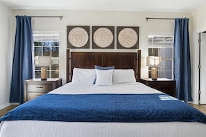 Un dormitorio con una cama grande, cabecero de madera oscura, paneles decorativos en la pared y vistas a través de una ventana con cortinas.