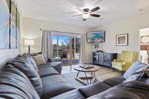 Ein Wohnzimmer mit einer Couch, einem Couchtisch, einem gelben Sessel, einem Deckenventilator und einem Fernseher.