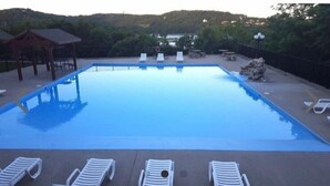 En rektangulär swimmingpool med kristallklart blått vatten, omgiven av solstolar och en pergola.
