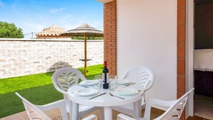 A patio with a round table set for dining, white plastic chairs, a bottle of wine, and glasses on the table. - Cozy Casa Torre de Meca 1 with Pool, Terrace, and Garden (Los Caños de Meca)